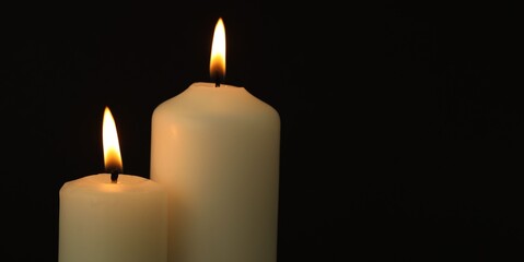 Two burning candles on black background, closeup. Space for text