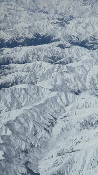 Incredible aerial view flying over a vast and majestic mountain range. The rugged terrain and sharp peaks are completely covered in white snow