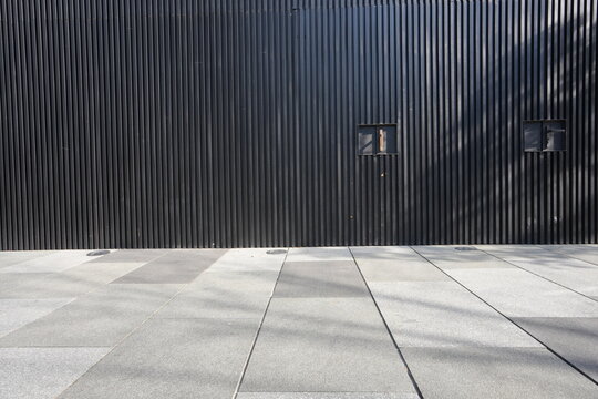 Black vertical corrugated metal wall with gray concrete pavement tiles