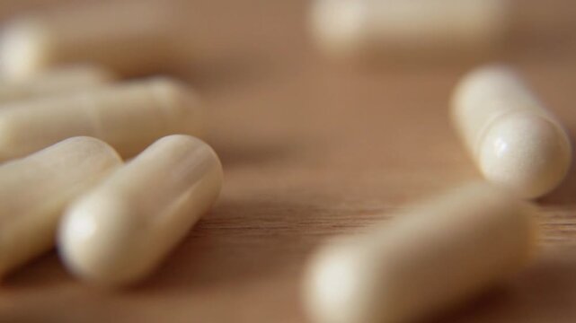macro close up of many white vitamin capsules falling and scattering on light wooden table surface in slow motion for pharmacy and healthcare background