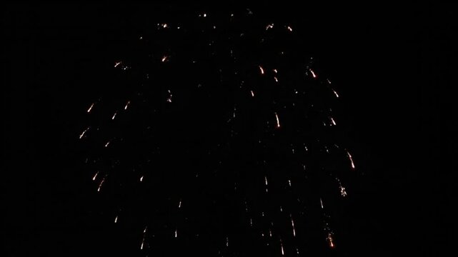 A single vibrant red firework bursts and fades against the deep black night sky, leaving trails of light.
