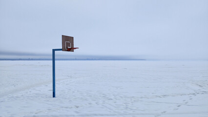 A solitary basketball hoop stands on a vast frozen, snow-covered plain. Minimalist composition with a cold, blue and white palette. Evokes feelings of solitude, quiet, and surreal absurdity © Анатолий Еремин