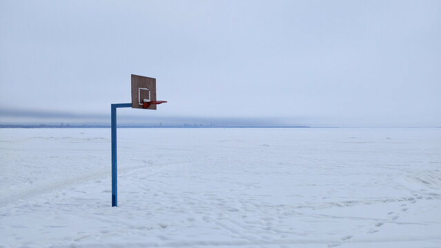 A solitary basketball hoop stands on a vast frozen, snow-covered plain. Minimalist composition with a cold, blue and white palette. Evokes feelings of solitude, quiet, and surreal absurdity