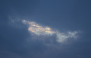 Obraz premium Sun shining through a gap in dark dramatic stormy clouds in the blue sky, silver lining concept.