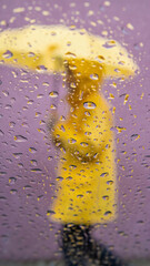 Woman in yellow raincoat holding matching umbrella walks in spring rain through water-streaked window. Vernal equinox weather with blurred purple backdrop symbolizing seasonal renewal and fresh