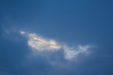 Fototapeta premium Sun shining through a gap in dark dramatic stormy clouds in the blue sky, silver lining concept.