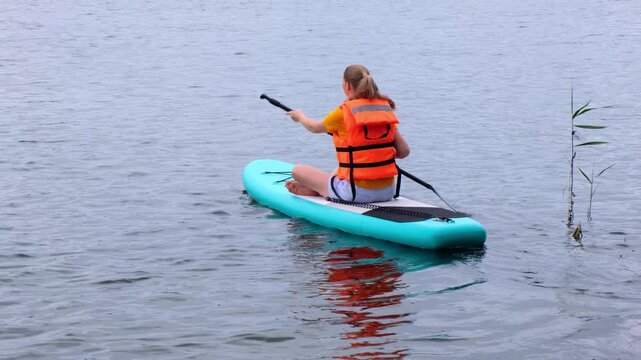 Woman paddling a stand up paddleboard on a lake outdoors. water sport, active leisure, summer vacation, nature fitness, calm water
