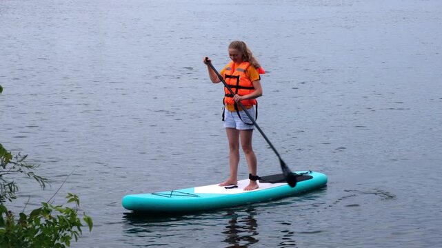 Woman standing on a stand up paddleboard on a lake outdoors. water sport, active leisure, summer vacation, nature fitness, calm water.