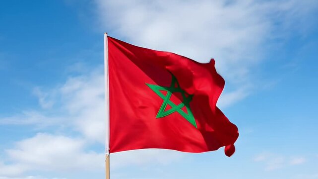 National flag of Morocco waving in wind against blue sky with white clouds in slow motion cinematic footage