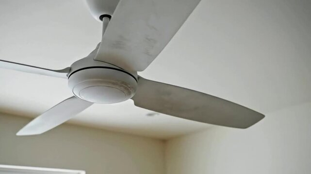 A dusty white ceiling fan spinning slowly in a bright room