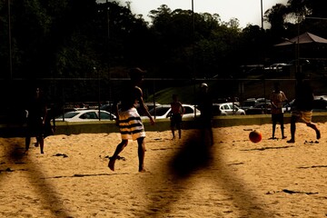 Meninos jogando futebol em campo de terra no p&ocirc;r do sol. 
