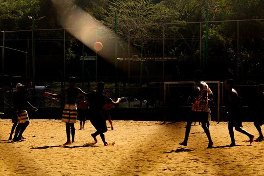 Meninos jogando futebol em campo de terra no p&ocirc;r do sol. 