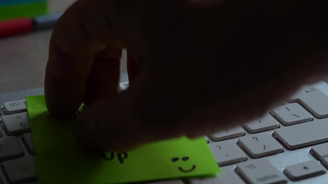 "Never Give Up" green sticky note left on keyboard. The bright note stands out against the keys, symbolising motivation, productivity, and a focused mindset. Shot in 4K, slow-motion, 50FPS.