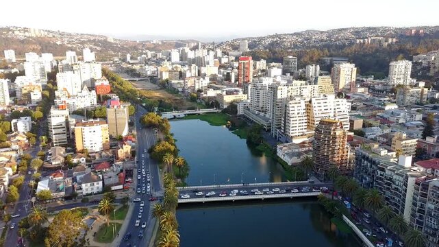 Aerial drone footage of a modern city with bridges crossing an urban river, surrounded by residential buildings and palm trees. Filmed above the Estero Marga Marga in Vina del Mar during golden hour.