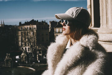 Stylish woman in fur coat and cap enjoying a sunny day outdoors