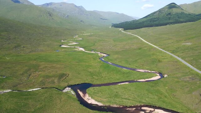 une rivi&egrave;re dans une vall&eacute;e verte avec une route au milieu des highlanders