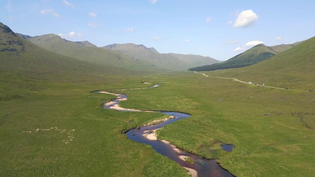 survol d'une rivi&egrave;re qui serpente dans une vall&eacute;e entour&eacute;e de montagne en Ecosse