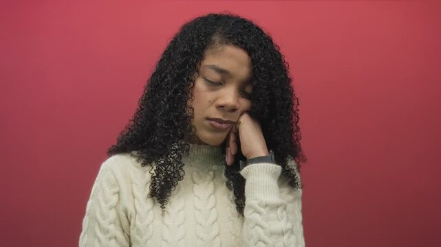 Woman leaning head on hand in studio wearing a white cable knit sweater and curly hair with closed eyes; boredom.
