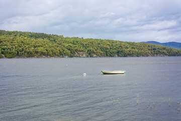 Fototapeta premium Lake surrounded by dense forest with a small solitary boat floating calmly on the water, suggesting a serene and tranquil atmosphere
