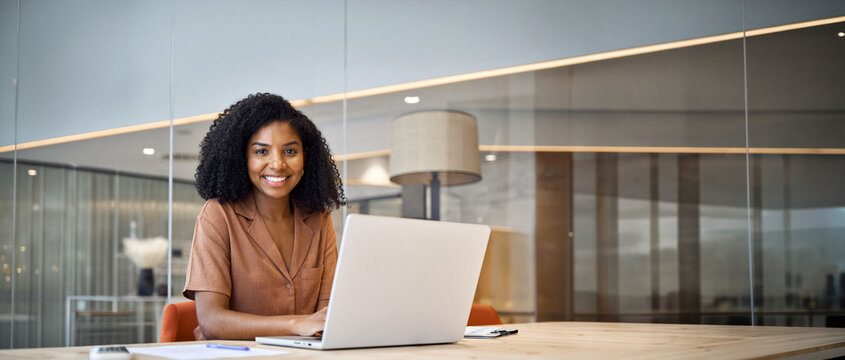Portrait of happy young African American business woman employee using laptop computer at work in office. Professional smiling businesswoman executive, company worker manager looking at camera.