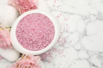 Obraz na płótnie Canvas Pink sea salt in bowl, spa stones and flowers on white marble table, flat lay. Space for text