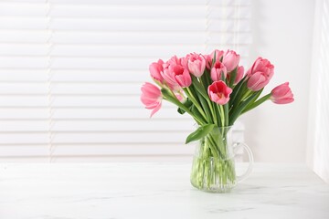 Fototapeta premium Bouquet of pink tulips in vase on white marble table. Space for text