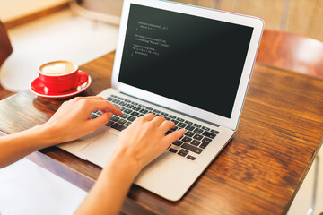 closeup of young woman's hands working on laptop computer programing projects in a cozy cafe setting
