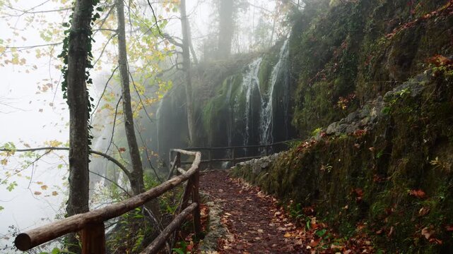 Misty trail leading past a cascading waterfall in a tranquil forest on an autumn day. Plitvice Lakes National Park, Croatia