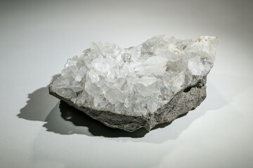 A part of a quartz druse on a base rock against a white background.
