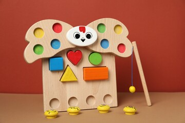 Obraz premium Magnetic sorting set for children with wooden hen, figures and fishing rod on beige table against brown background, closeup