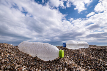 Obraz premium Environmental Pollution – Discarded Plastic on Sand. Plastic Waste Bottles on Sandy Beach. Plastic Trash on Sand Highlighting Environmental Issue. Coastal Pollution with Abandoned Plastic Waste.