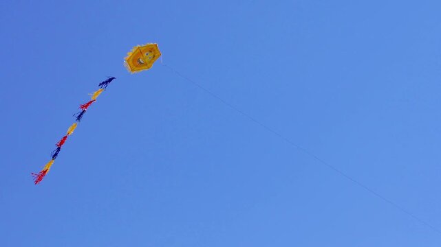 Group of kites flying and gently swaying with long ribbons in wind against bright blue sky during sunny spring day
