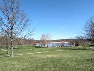 Obraz premium Wide Open Park with Lake and Clear Blue Sky, Early Spring Landscape Background