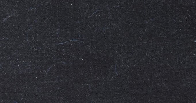 Stop-motion style close-up of dark black handmade paper with visible fibers, lint, and tiny specks. Moody textured background for design overlays, transitions, or looping footage.