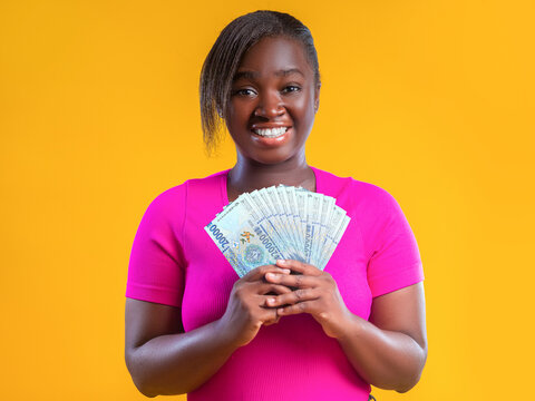 A happy woman in a pink t-shirt smiles against a yellow background, holding a fan of 20,000 Guinean Franc banknotes. The image captures themes of financial success and prosperity in Guinea.