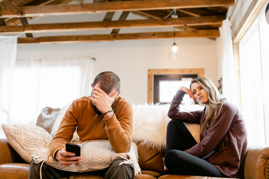 Unhappy Couple Sit Together on Couch, Man on Phone