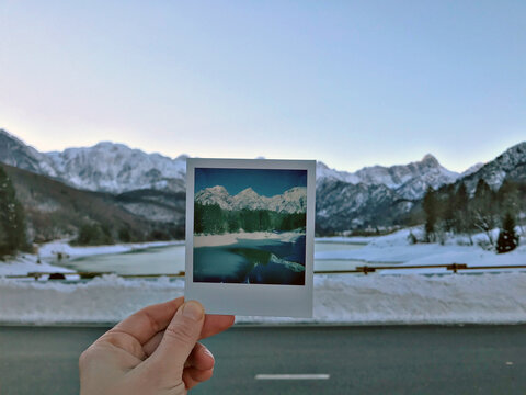 Hand Holding an Instant Photo Framing a Snowy Mountain View
