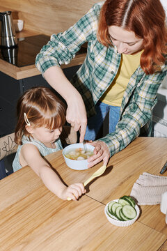 Mother stirs up soup for her daughter in the kitchen.