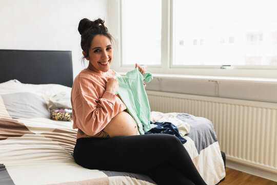 Future mom looking at baby clothes in bedroom
