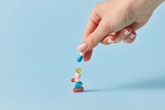 Person placing white and blue capsule on stack of pills