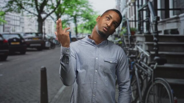 Black man points finger to temple and shows middle finger on a street lined with bicycles and parked cars; defiance urban attitude.