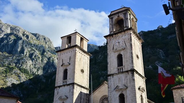 Cathedral of Saint Tryphon bell towers standing against a backdrop of steep mountains under a blue sky