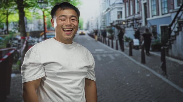 Man gestures with hands on a sunlit urban street while wearing a casual white tshirt and denim jeans; happiness.