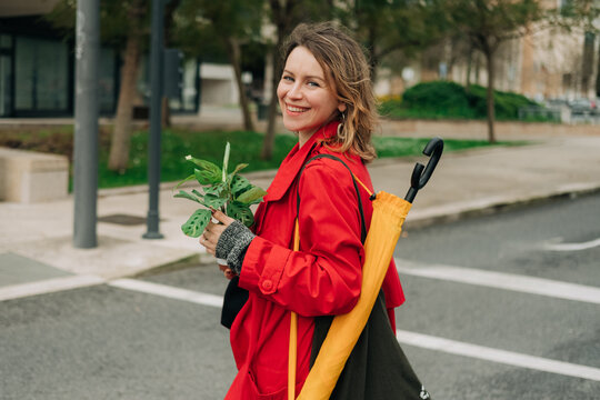 Woman walking with potted plant in hands, looking at camera with