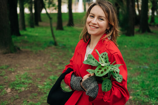 Woman smiling at camera while walking with a houseplant