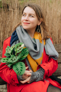 Woman sitting on a bench with a potted maranta plant in her hand