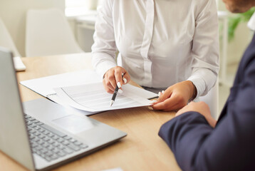 Cropped shot of two business people sitting at work desk with laptop, discussing financial data or terms of contract. Male and female colleagues or partners working with documents together in office.