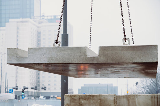Low-angle view of a prefabricated concrete slab suspended during crane installation. Urban construction environment highlighting modern infrastructure development.