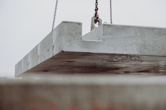 Large prefabricated concrete slab suspended by chains during crane operation. Heavy precast element positioned at an urban construction site.