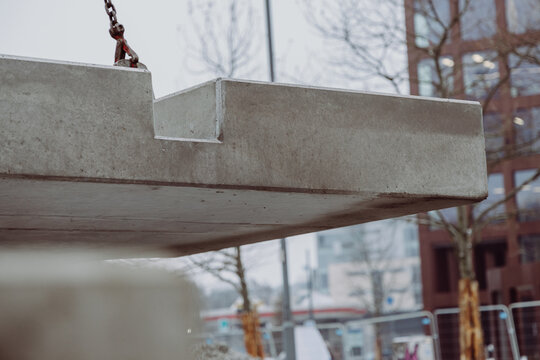 Prefabricated concrete slab lifted by crane above an urban construction area. Industrial building element prepared for installation in large-scale infrastructure